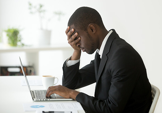 Employer Liability man covering his face with one hand, while his other hand is on his laptop