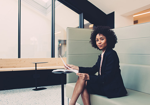 young lady in an office suit sitting on couch holding documents looking at the camera